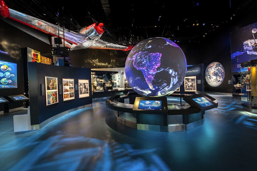 Dark exhibit with a glob and space ship that has interactive panels