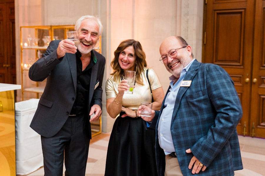 Three smiling attendees raise their glasses in a joyful toast at an elegant gathering.