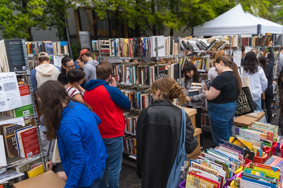 Shoppers browse outdoor book racks during the Georgetown French Market surrounded by colorful displays and tents.