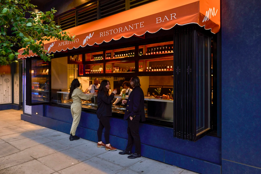 The exterior of a restaurant with a bright orange awning, with people gathered outside the sleek, open-air bar. 