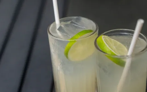 A. closeup of two tall glasses with limes and straws. 