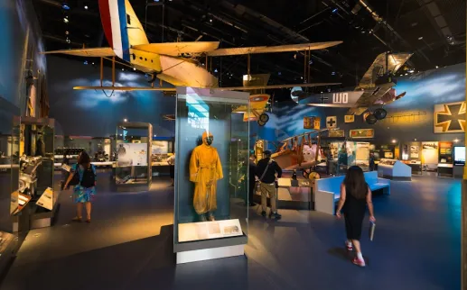 Visitors walk through an aviation exhibit with vintage aircraft and a yellow flight suit on display.

