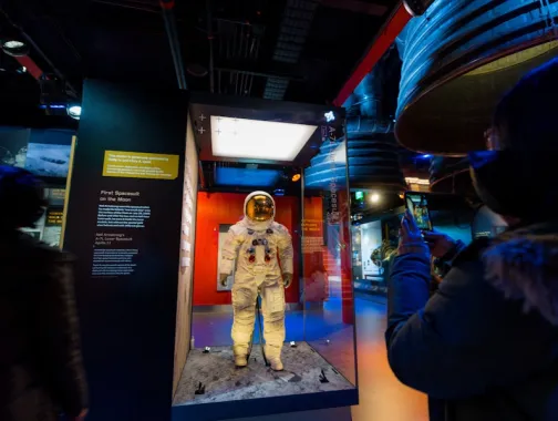 A visitor takes a photo of Neil Armstrong’s Apollo 11 spacesuit on display behind glass.