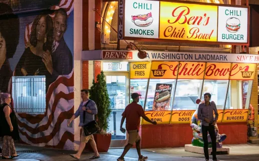 People walk by Ben's Chili Bowl at night. 

