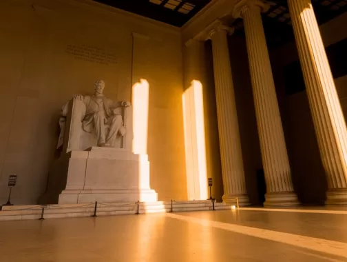 The statue of Abraham Lincoln bathed in golden light inside the Lincoln Memorial.