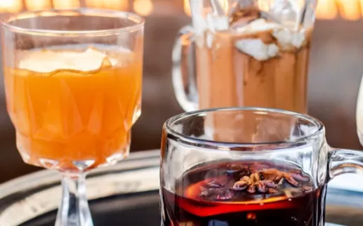 A collection of cozy winter cocktails on a plater in front of a fire. 