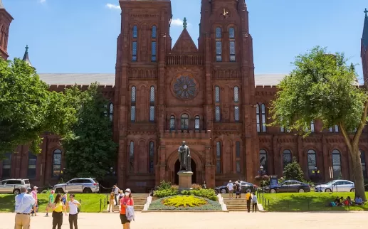 Visitors stroll across the sunny lawn in front of the iconic red sandstone Smithsonian Castle on the National Mall.
