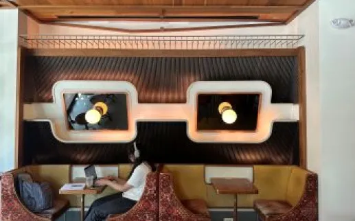 A person wearing headphones works at a booth in a stylish café with retro lighting and mid-century modern decor.
