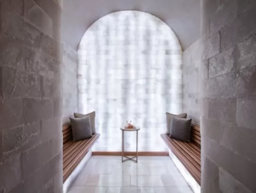 Himalayan Salt Therapy Room at Waldorf Astoria Washington DC, featuring wooden benches, pillows, and a small table with spa items.